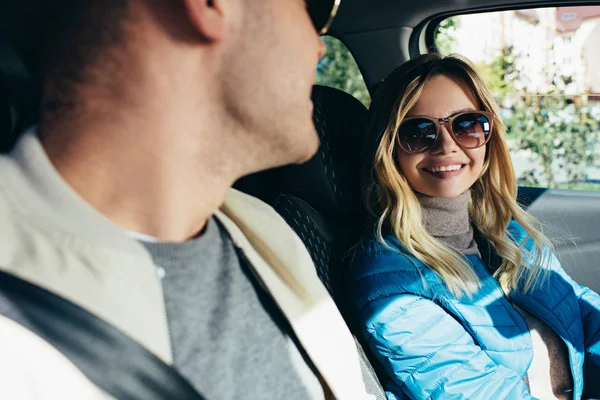 Sonriente mujer en gafas de sol mirando novio en coche - foto de stock