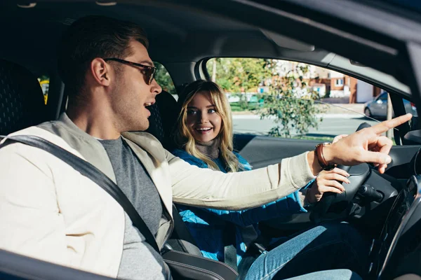 Side view of man pointing way to girlfriend on drivers seat in car — Stock Photo