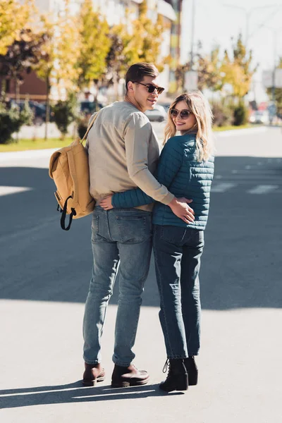 Back view of couple hugging and looking at camera while walking on street in new city — Stock Photo