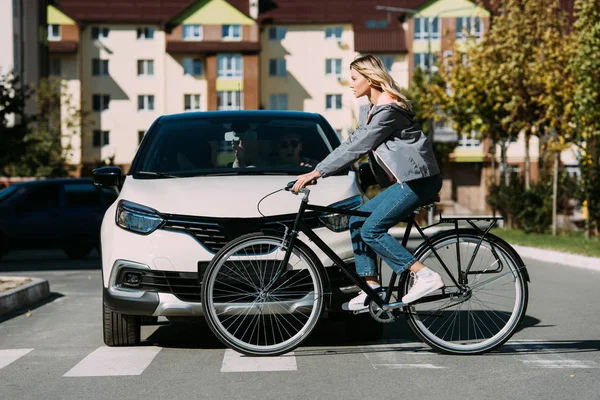 Mulher andar de bicicleta enquanto atravessa a estrada com o motorista no carro — Fotografia de Stock
