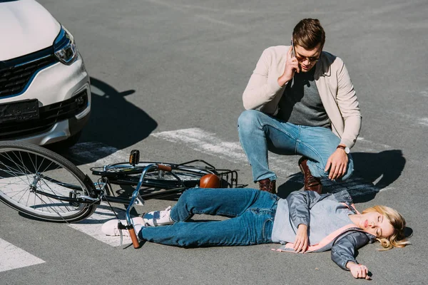 Young man near injured woman calling ambulance after car accident on road — Stock Photo