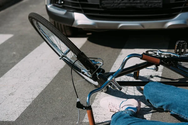 Vista parcial de la mujer con la bicicleta segada por el coche en la carretera, concepto de accidente de coche - foto de stock