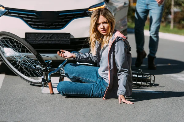 Partial view of injured woman on road after car accident with car driver behind — Stock Photo