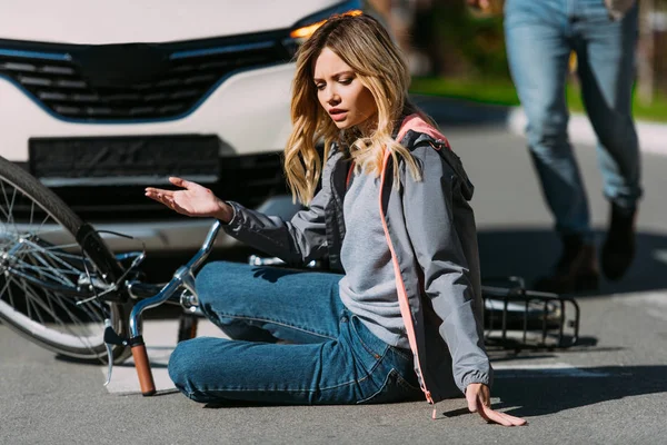 Partial view of injured woman on road after car accident with car driver behind — Stock Photo