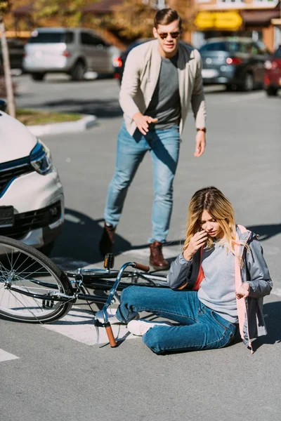 Selective focus of injured woman on road after car accident with car driver behind — Stock Photo