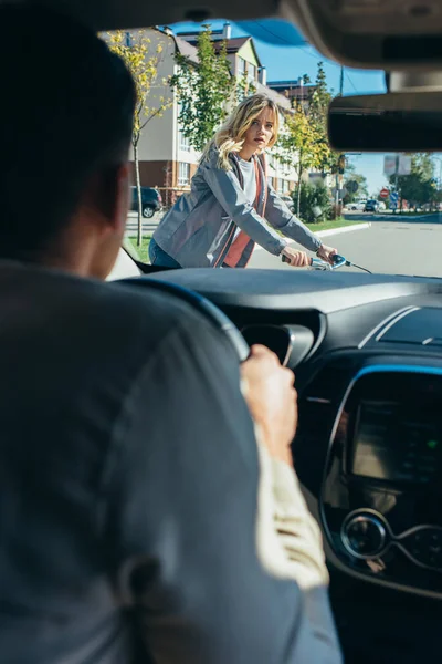Car driver waiting while young woman on bicycle crossing road — Stock Photo