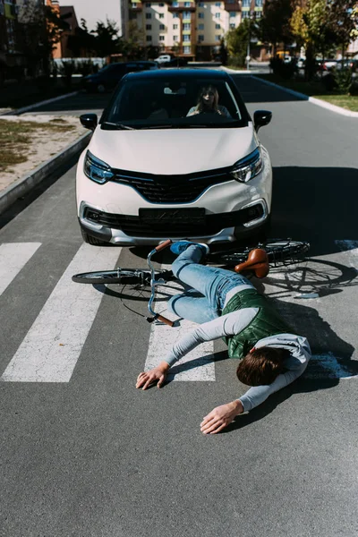 Ciclista masculino golpeado por la mujer en el coche en la carretera, concepto de accidente de coche - foto de stock