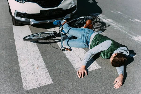 Ciclista masculino golpeado por el coche en la carretera, concepto de accidente de coche - foto de stock