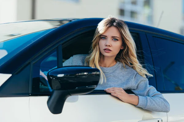 Portrait of young blond woman looking at camera while driving car — Stock Photo