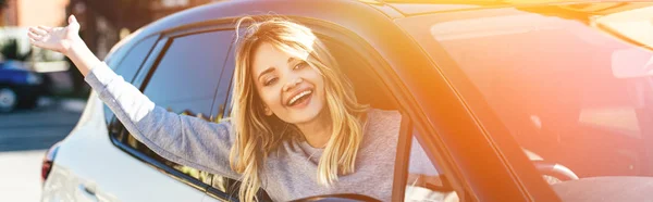 Portrait of happy blond woman waving to someone while driving car — Stock Photo