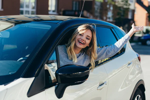 Portrait d'une femme blonde heureuse saluant quelqu'un en conduisant une voiture — Photo de stock