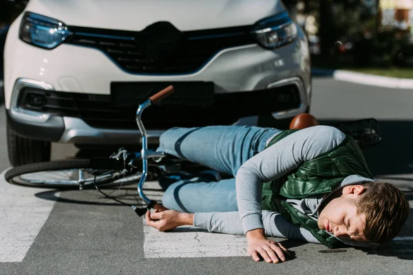 Injured cyclist lying with bicycle on road after motor vehicle collision — Stock Photo