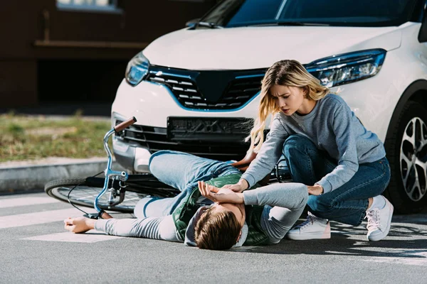 Young woman trying to help injured cyclist at car accident — Stock Photo