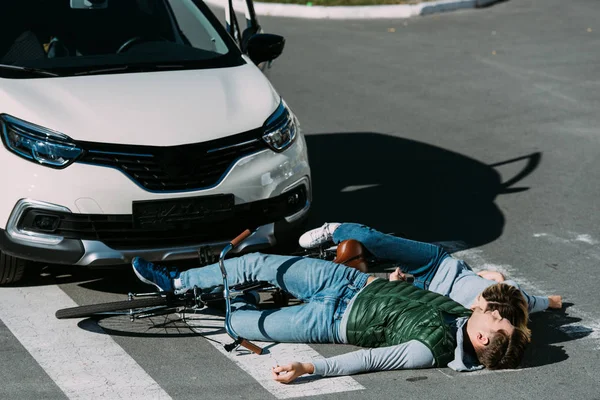 Jóvenes ciclistas acostados en la carretera en el accidente de coche - foto de stock