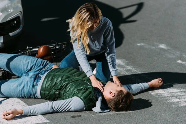 Mujer joven comprobando el pulso del ciclista lesionado después de una colisión de tráfico - foto de stock