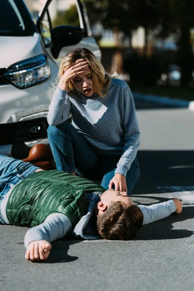 Shocked young woman looking at injured young cyclist lying on road after traffic collision — Stock Photo