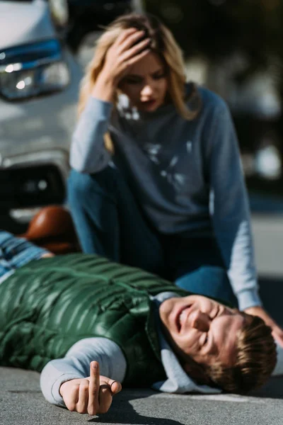 Injured young man lying on road and showing middle finger after traffic collision — Stock Photo