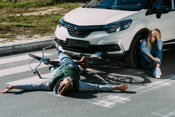 Vue grand angle du cycliste couché sur la route et de la femme effrayée pleurant près de la voiture après une collision de la circulation — Photo de stock