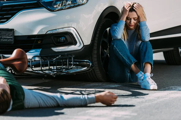 Recortado disparo de ciclista acostado en la carretera y mujer asustada llorando después de la colisión de tráfico - foto de stock