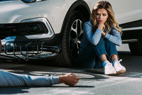 Cropped shot of cyclist lying on road and scared woman sitting near car after traffic collision — Stock Photo