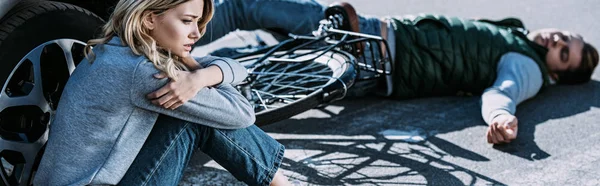 Young woman sitting near car and victim of traffic accident lying on road — Stock Photo