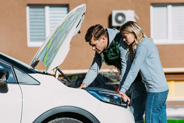 Side view of young couple fixing broken car on street — Stock Photo