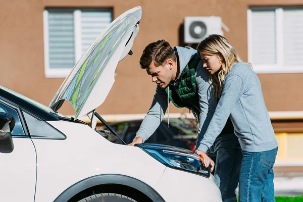 Seitenansicht eines jungen Paares, das kaputtes Auto auf der Straße repariert — Stockfoto