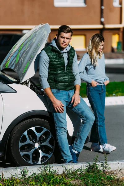 Chateado jovem casal perto de carro quebrado na rua — Fotografia de Stock