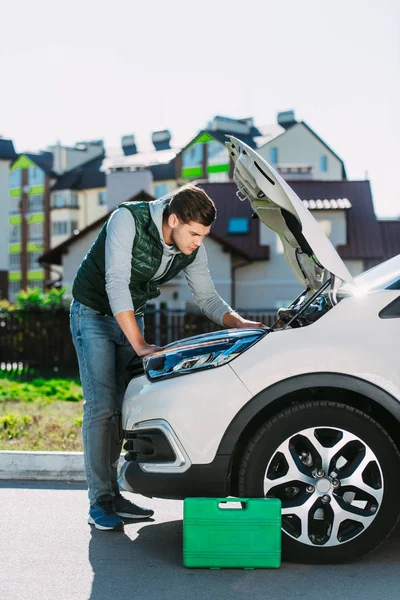 Seitenansicht eines fokussierten jungen Mannes, der kaputte Autos auf der Straße repariert — Stockfoto