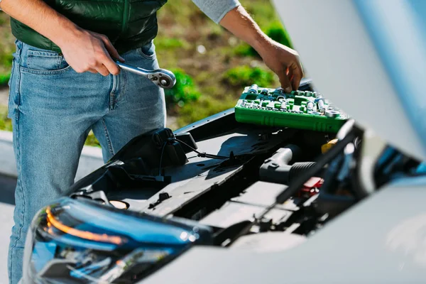 Cropped shot of young man with tools repairing broken car — Stock Photo