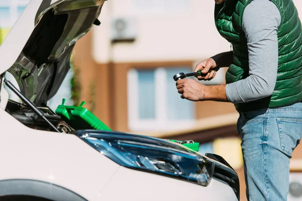 Colpo ritagliato di uomo che tiene la chiave inglese e fissa l'auto rotta — Foto stock