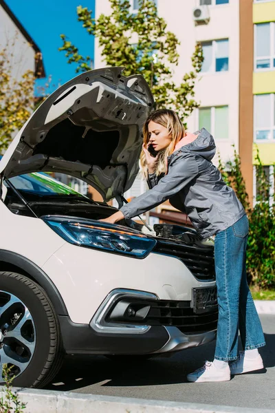 Mujer joven hablando por teléfono inteligente y reparación de coches rotos - foto de stock