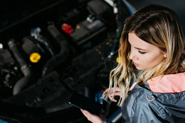 Високий кут зору молодої жінки за допомогою смартфона з порожнім екраном під час ремонту зламаного автомобіля — стокове фото