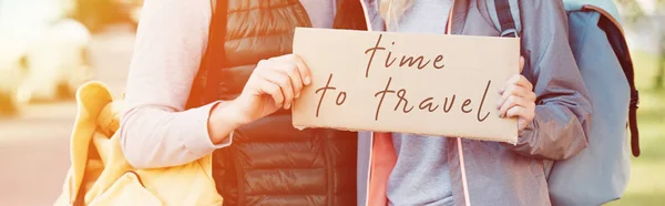 Cropped shot of young couple with backpacks holding card with inscription time to travel — Stock Photo