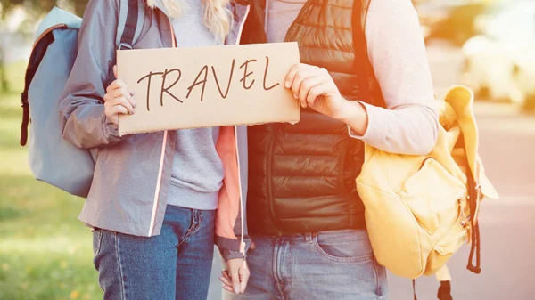 Tiro recortado de jovem casal com mochilas segurando cartão com viagem inscrição — Fotografia de Stock
