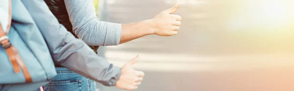 Cropped shot of young couple hitchhiking on road at sunset — Stock Photo