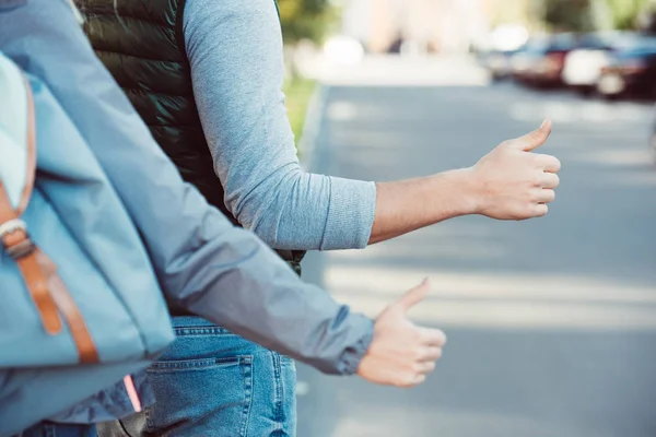 Cropped shot of young couple of travelers hitchhiking on road — Stock Photo