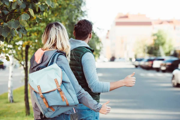 Back view of young couple hitchhiking on road — Stock Photo