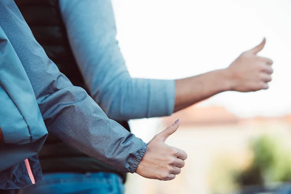 Close-up partial view of young couple hitchhiking on road — Stock Photo