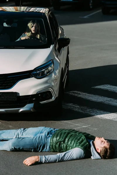 Vue en angle élevé du jeune homme blessé allongé sur la route après un accident de voiture — Photo de stock