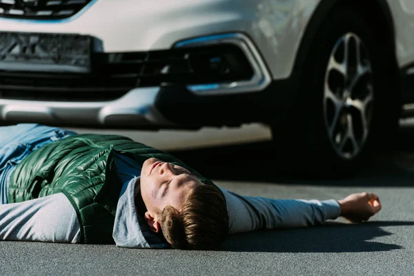 Nahaufnahme eines verletzten jungen Mannes, der nach einem Autounfall auf der Straße liegt — Stockfoto