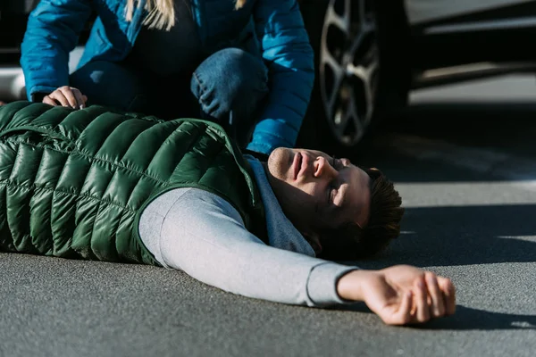 Coup de feu recadré de la femme touchant jeune homme blessé couché sur la route après un accident de voiture — Photo de stock