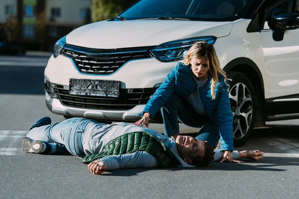 Mujer joven mirando a la víctima de colisión de tráfico acostado en la carretera - foto de stock