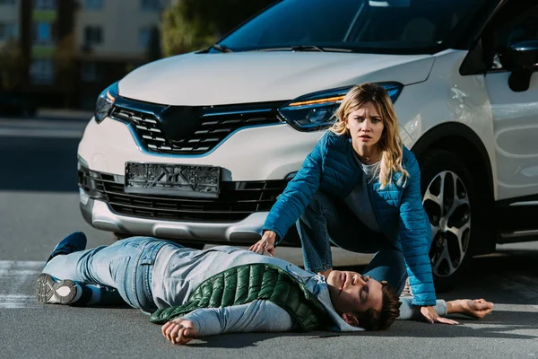 Young woman looking at camera while touching victim of motor vehicle collision — Stock Photo