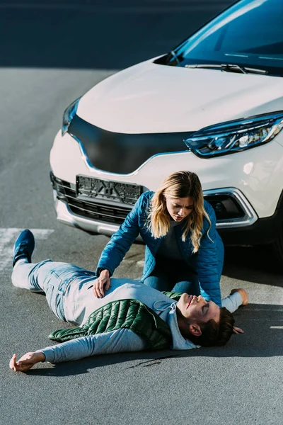 Vue en angle élevé de la jeune femme regardant toucher un homme blessé allongé sur la route après un accident de la circulation — Photo de stock