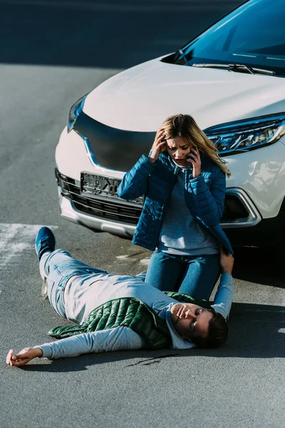 Jeune femme effrayée regardant l'homme blessé et appelant d'urgence après un accident de voiture — Photo de stock