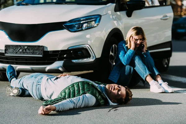 Verängstigte junge Frau ruft Notruf, während verletzter Mann nach Verkehrsunfall auf der Straße liegt — Stockfoto