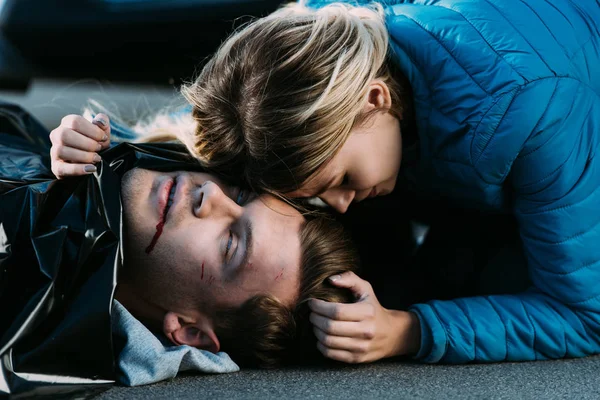 Vista de cerca de la mujer joven llorando y abrazando al hombre muerto en la carretera después de una colisión de tráfico - foto de stock