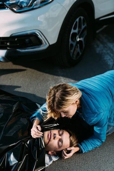 Vista de ángulo alto de la mujer joven llorando sobre el hombre muerto en la carretera después de la colisión de tráfico - foto de stock