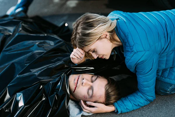 Mujer joven llorando y mirando al hombre muerto en el camino - foto de stock